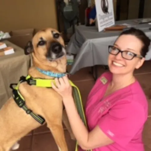 A staff member at Pinnacle Peak Animal Hospital smiling and posing with a large tan dog